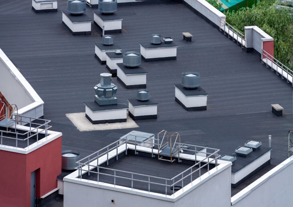 Top view flat roof with air conditioners and hydro insulation membranes on top of a modern apartment building summer day. built up roofing
