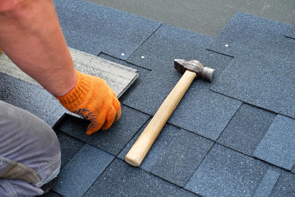 how to install architectural shingles-close up of man wearing gloves installing dark gray architectural shingles