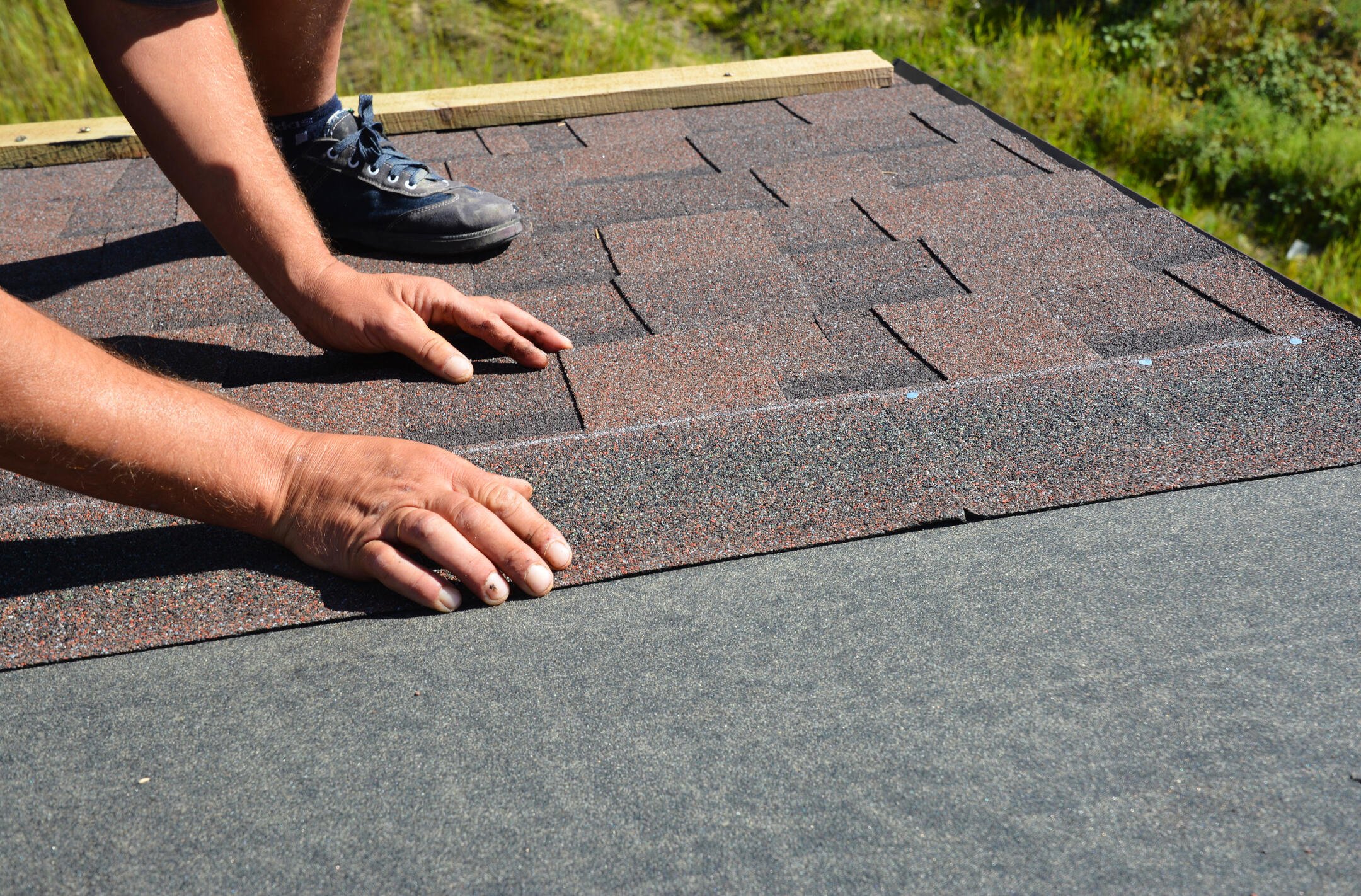 how to install architectural shingles-close up view of a person installing brown architectural shingles on a house roof
