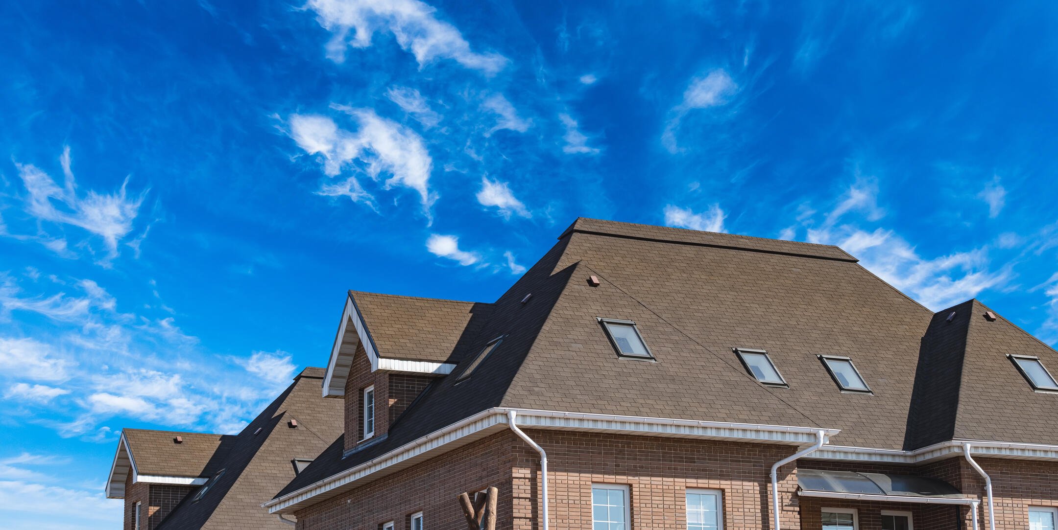 layers of a roof-brick home with a shingle roof with a blue sky background