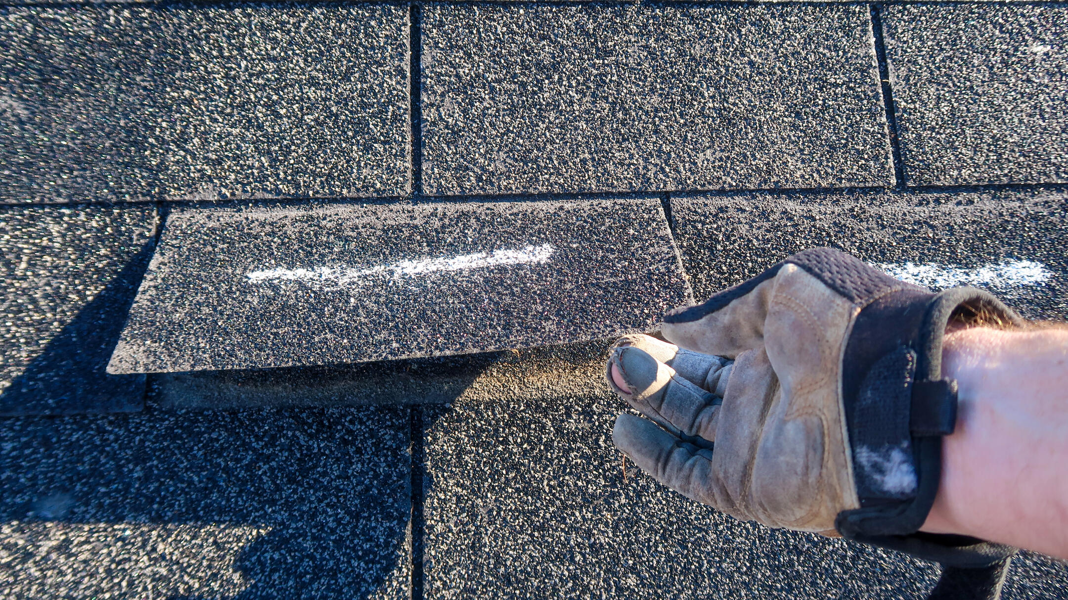 repair or replace roof-gloved hand lifting a roof shingle