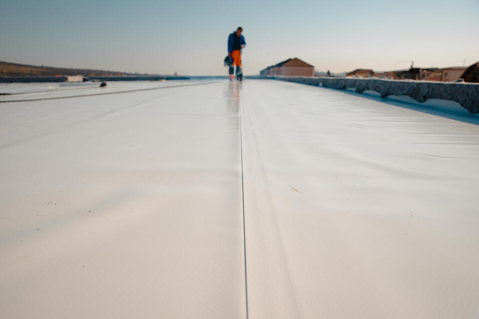 flat roof repair-low distant view of roofer installing pvc roofing