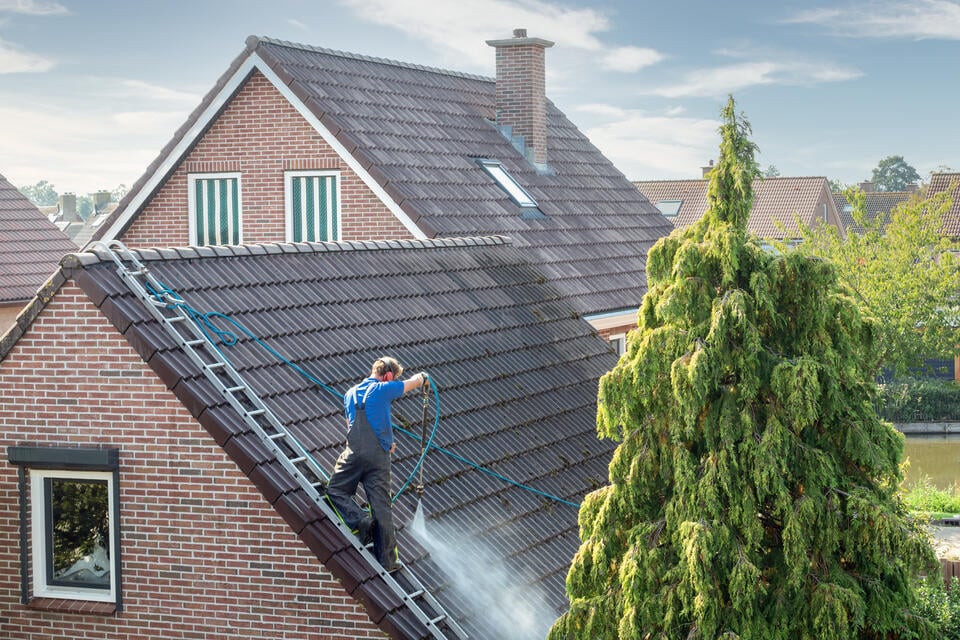 how to clean roof shingles-distant view of man power washing roof shingles