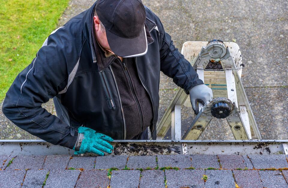 how to clean roof shingles-man prepping roof to be cleaned by clearing gutters