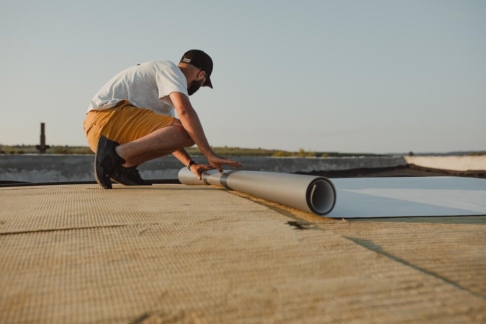 pvc roofing-man unrolls pvc membrane on flat roof
