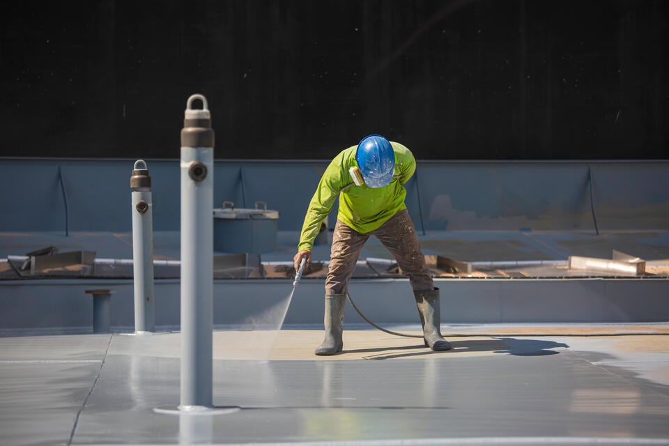 roof coating-man wearing protective gear spraying on roof coating