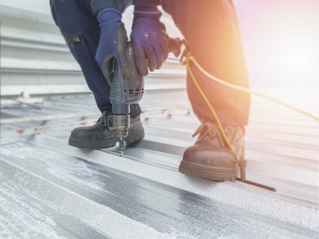 worker screwing in metal seam roof commercial building