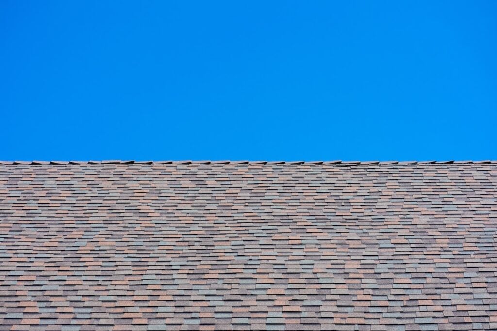 Laminated architectural roof shingles of different shapes and sizes give the rooftop dimensional appearance. Blue sky.