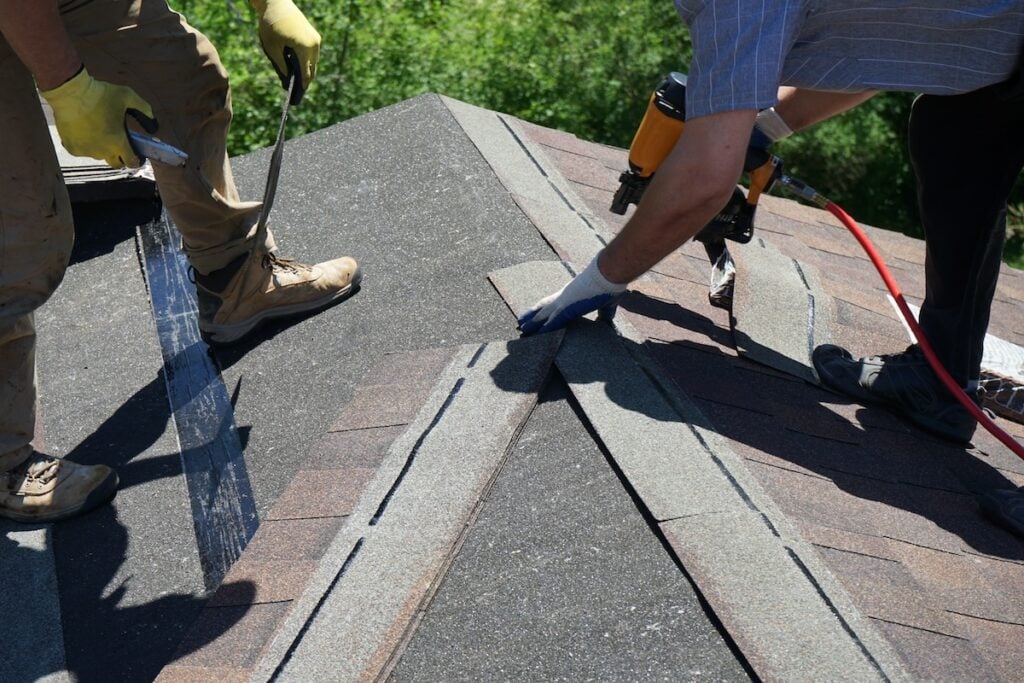 View of two workers on the roof with Roofing nail gun installing Asphalt Shingles.