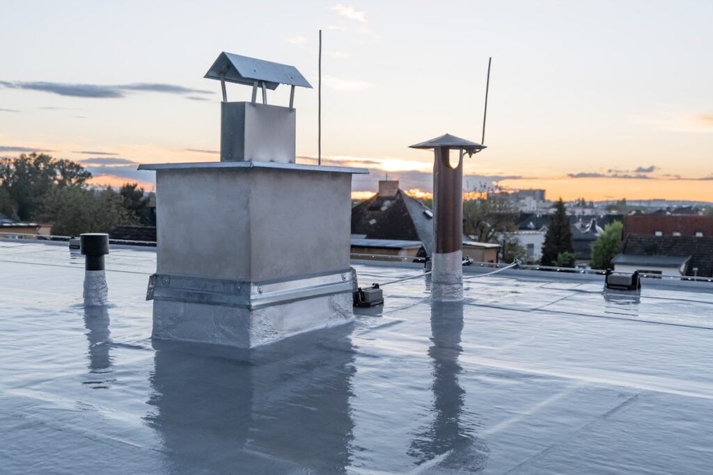 Flat roof covered with bitumen membrane and silver lacquer with chimney on a private house. Reflections after rain