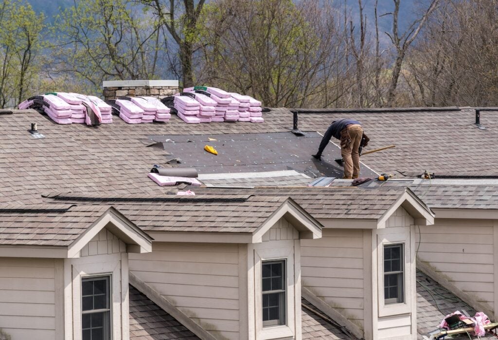 Roofing contractor removing the old tiles before replacing with new shingles on a townhouse roof