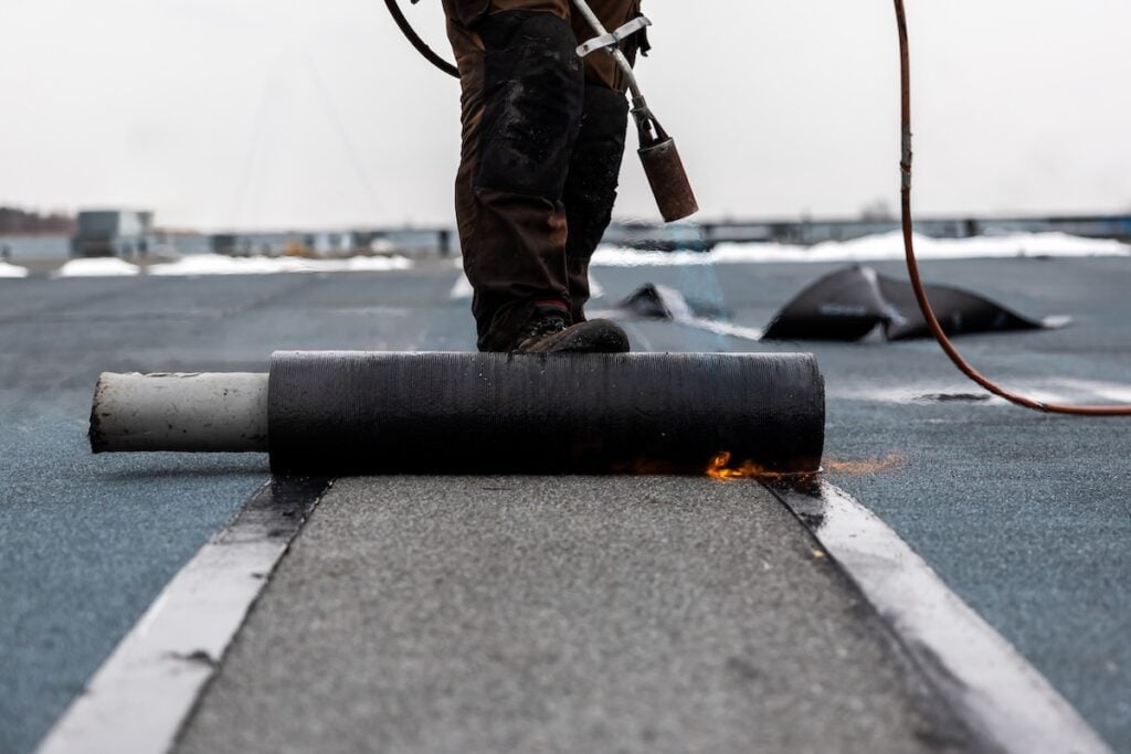 professional roofer at work securing rolled tar paper with a blowtorch on a flat roof installation process rubber roof repair