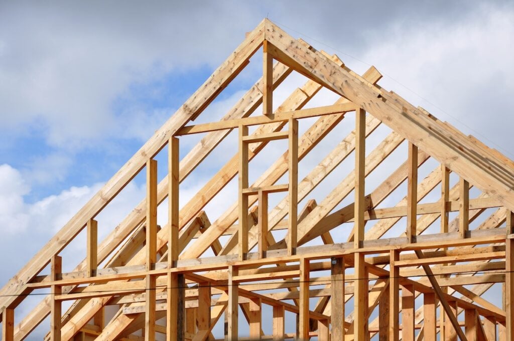 The process of construction of a frame private house with a pitched roof. Wooden frame on the blue sky background.