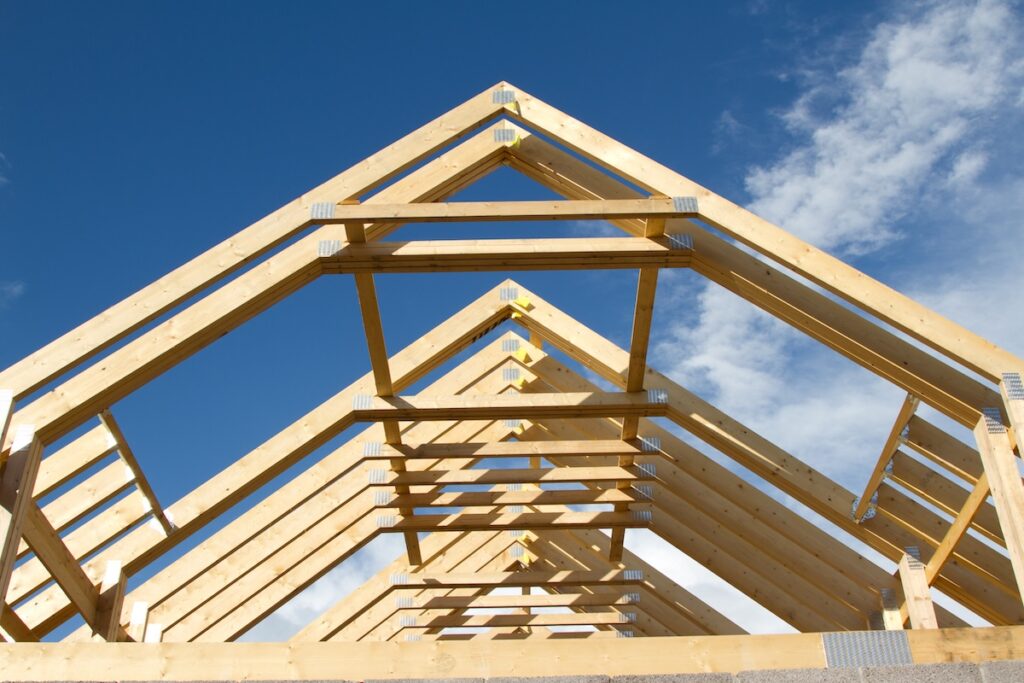 A new build roof with a wooden truss framework making an apex against a blue sky with cloud