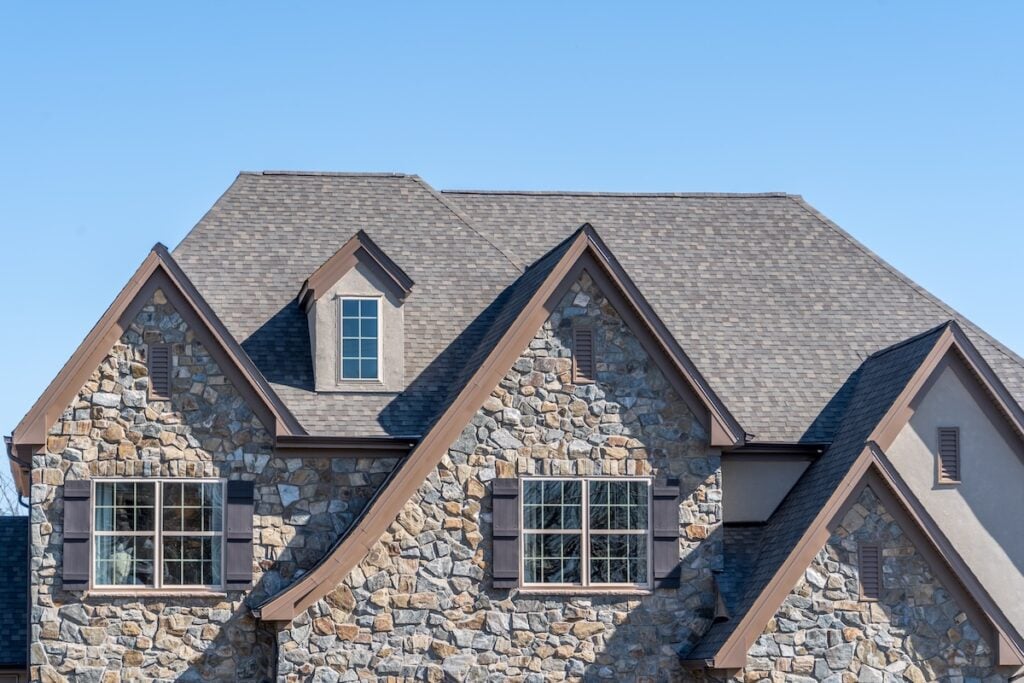 Double gable with dark stone veneer siding, with triangle shape peaks, on a pitched roof attic at an American single family home neighborhood USA, double sash windows w/ matching dark shutters