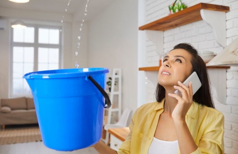 Sad unhappy frustrated young housewife lady looking up at water falling down from damaged ceiling in newly renovated home interior, holding pail and speaking to repair service. House roof leak concept