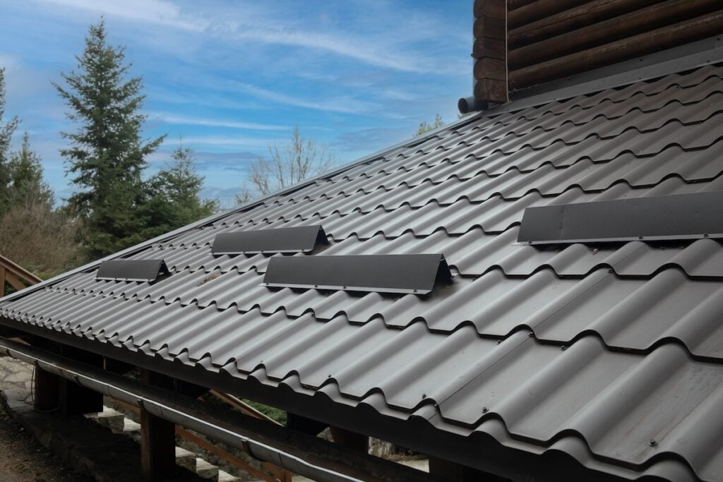 cost of metal roof vs shingle Closeup roof with metal grey shingle tiling surface with rain gutter pipe and snow guards protective fence.