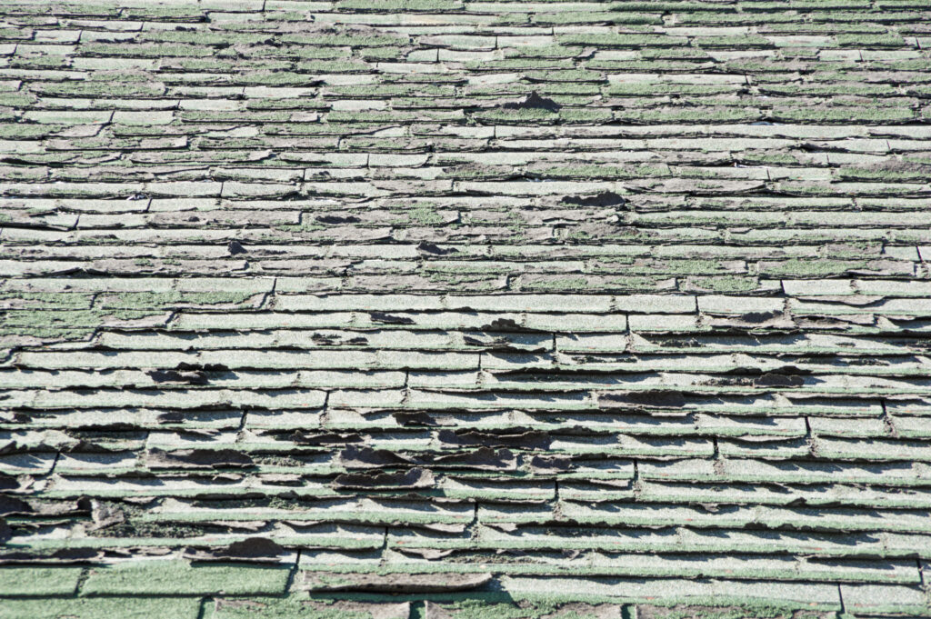 sun damaged old roof with peeling and curling composition shingles