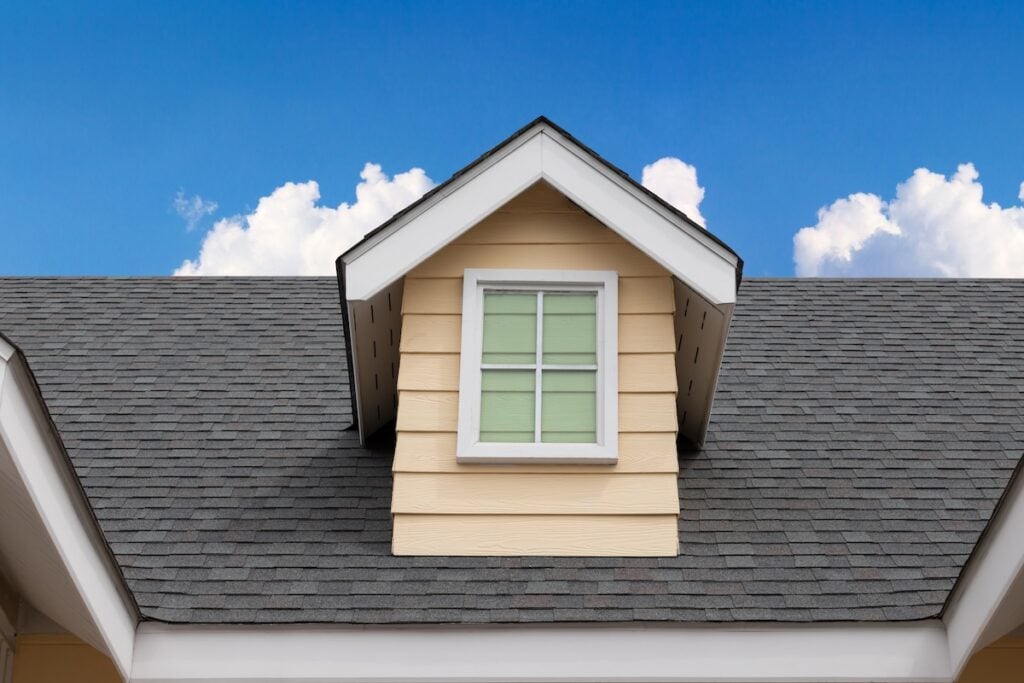 black streaks on roof fake window on garret house and roof shingle wirh blue sky background. Asphalt Shingles or Bitumen Tiles.