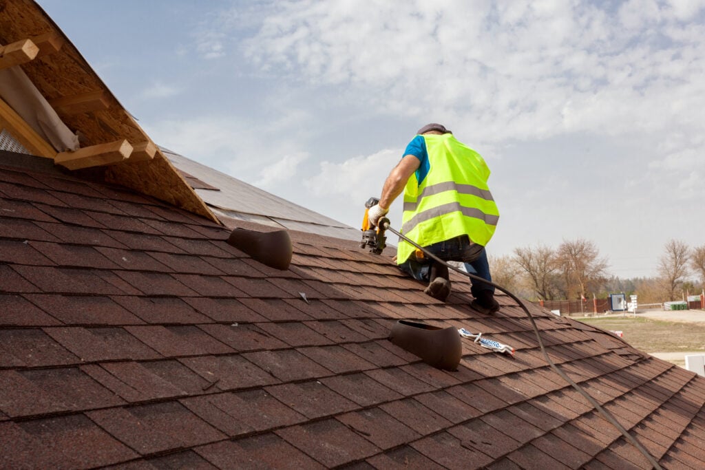 roofing companies Bethany ok Construction worker putting the asphalt roofing (shingles) with nail gun on a large commercial apartment building development