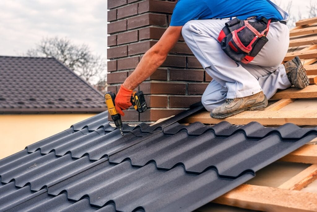 roofing companies mustang ok a professional master (roofer) with electric screwdriver covers repairs the roof near the chimney