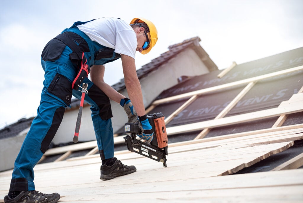 roofing companies Bethany ok The roofer is nailing wooden battens on the roof with electric nailer.