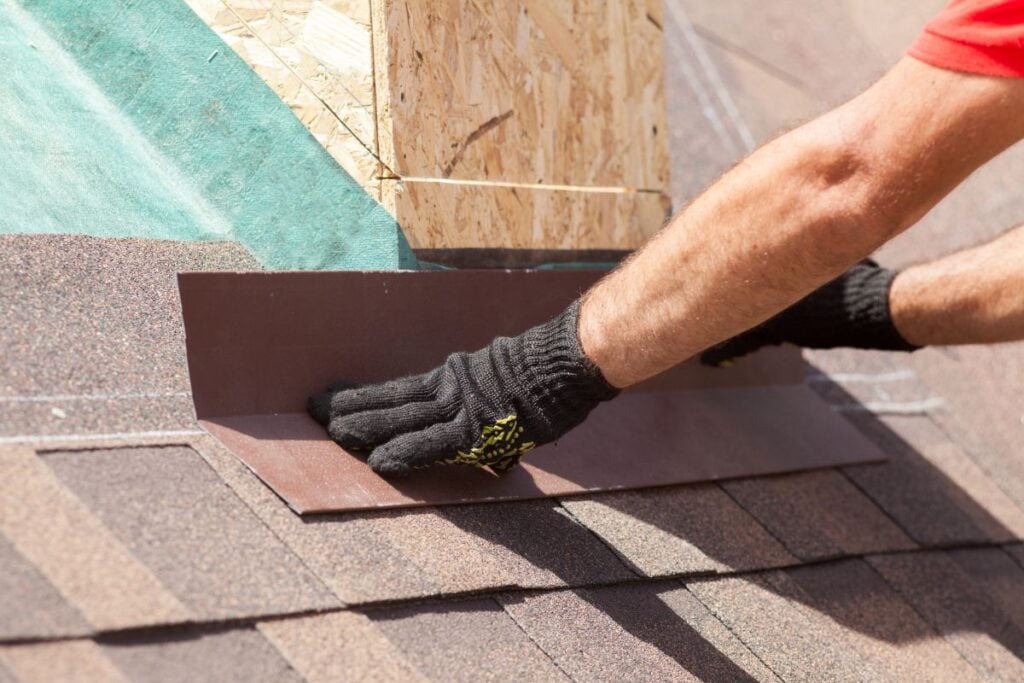 Roofer builder worker installing shingles on a new wooden roof with skylight