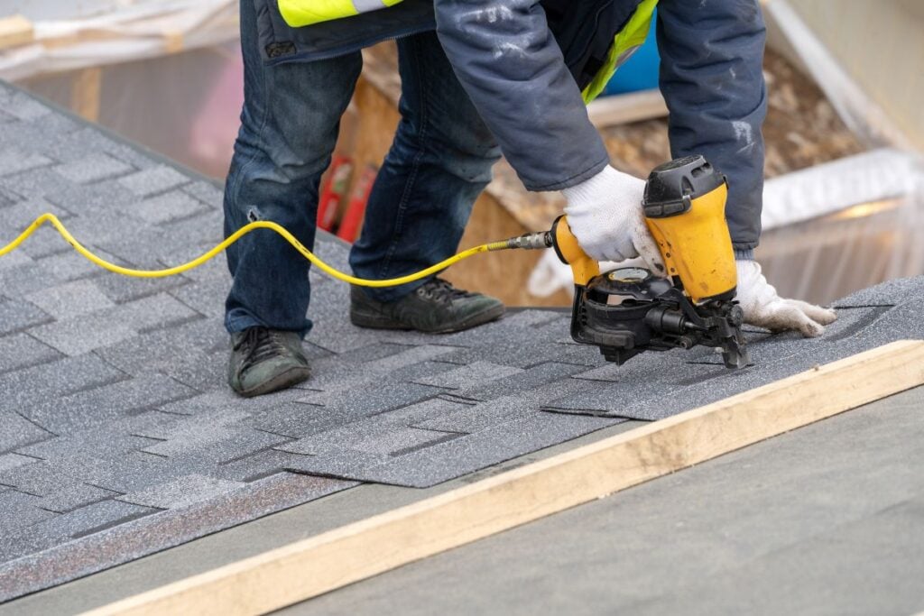 Workman using pneumatic nail gun install tile on roof of new house under construction