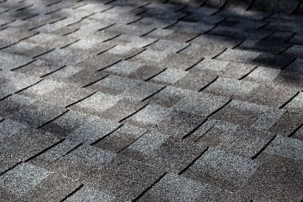close-up of an asphalt shingle roof at an angle with dappled sunlight
