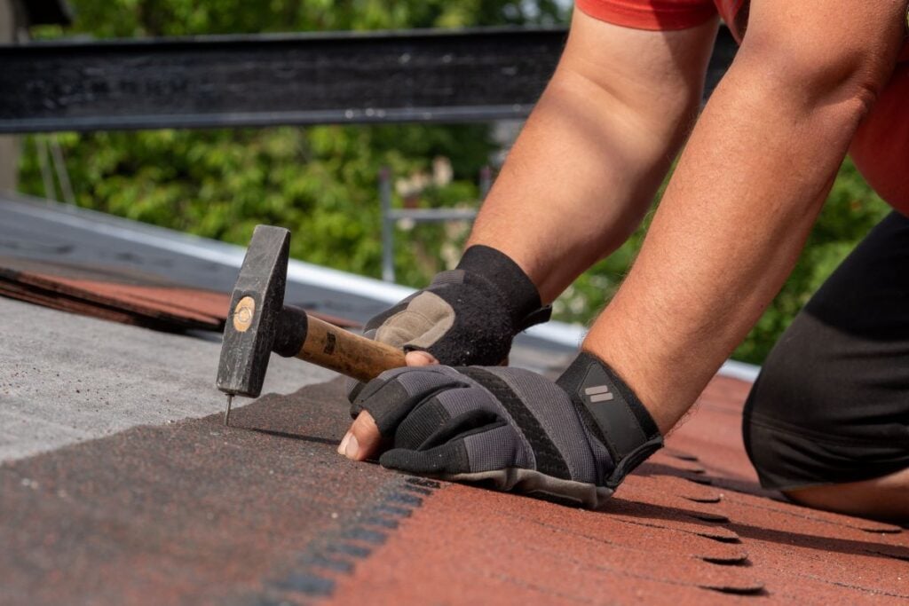 Roofer hands installing bitumen roof shingles using hammer in nails