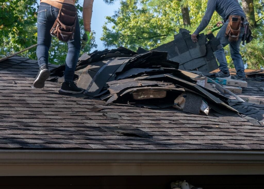 Roofers removing old material from a house in preparation for storm damage repair